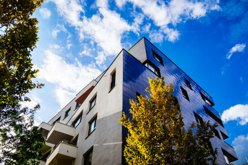 Modern residential building with reflective blue facade and geometric design under cloudy sky with...