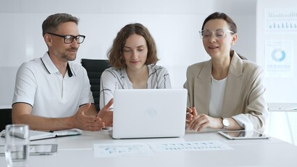 Professional team reviewing project data on laptop, working together in modern office environment, collaborating with focused corporate energy. Business people concept