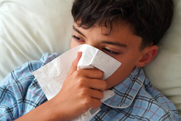 child health and well-being concept. child in pajamas with tissue and red eyes