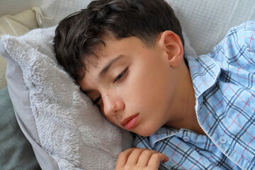 child health. Child in pajamas lying sick on the sofa with a look of discomfort or sadness.