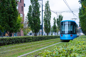 Blue tram on green track surrounded by trees in Oslo, clean energy public transport and sustainable mobility