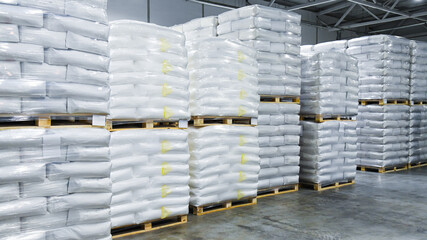 Large stacks of white bags, neatly stacked on wooden pallets and wrapped in transparent plastic.