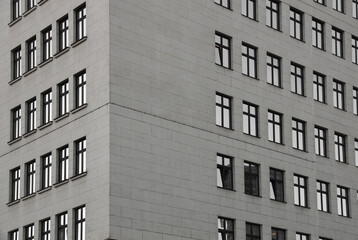 many rows of glass windows frames on large square grey concrete tiles wall of business office building. angle view. gray tiled exterior. Belgrade Serbia City centre Blue cloudy sky heaven
