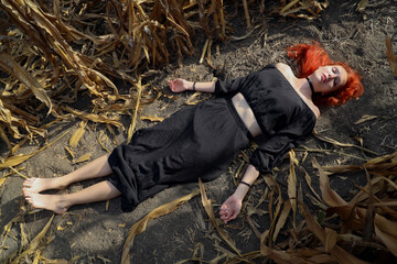 Young redhead barefoot lady female woman witch wear long black dress lying down in row middle of...