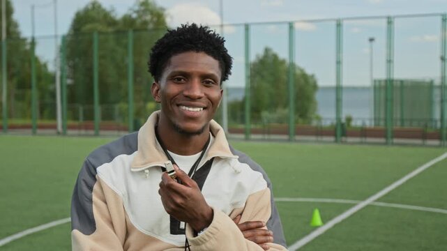Highly qualified African American coach blowing whistle and turning head to camera, he smiling making confidence impression