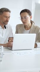 Fototapeta premium Businessman and adult businesswoman reviewing marketing analytics on laptops, working together strategically in contemporary office workplace. Business people concept