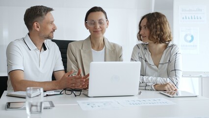 Professional team reviewing project data on laptop, working together in modern office environment, collaborating with focused corporate energy