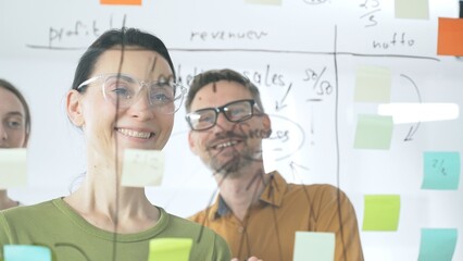 Professional team brainstorming project strategy, placing colorful sticky notes on glass board, analyzing data, sharing insights, developing collaborative solutions