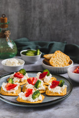 Appetizer of crackers with ricotta, cucumber and tomato on a plate on a table vertical view