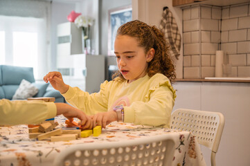Curly-haired girl picking up colorful wooden blocks after game collapse at home