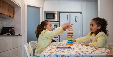 Twin sisters playing a colorful wooden block stacking game together in the kitchen