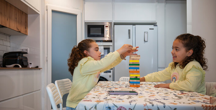 Twin sisters playing a colorful wooden block stacking game together in the kitchen