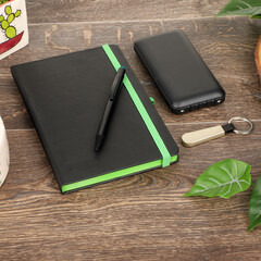 Black Notebook With Green Elastic, Pen, Phone Case, And Keychain On Wooden Desk;