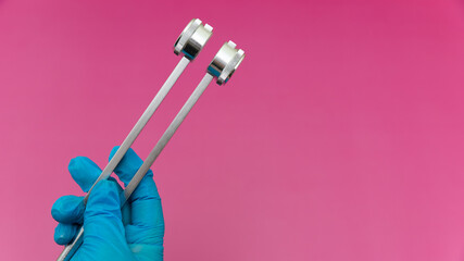 Blue Gloved Hands Holding tuning fork On pink Background, medical instruments in the hands of a...