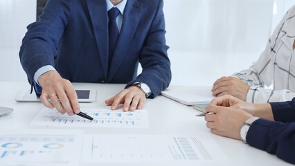 Business people engaging in a corporate meeting, discussing strategies while analyzing financial charts and graphs on a digital tablet alongside printed documents in office