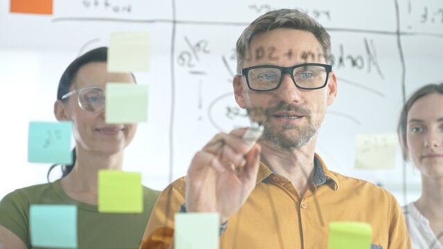 Professional team brainstorming project strategy, placing colorful sticky notes on glass board, analyzing data, sharing insights, developing collaborative solutions - Powered by Adobe