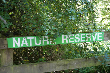 Green NATURE RESERVE sign on a weathered wooden fence surrounded by lush trees and red berries at Oakham Nature Reserve, Mansfield, Nottinghamshire, England