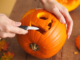Hands carving a Halloween pumpkin with a scary jack-o&rsquo;-lantern face.Perfect for illustrating Halloween traditions, pumpkin carving, and autumn lifestyle.