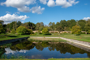 A landscape with a small lake surrounded by trees with reflection on water.
