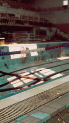 An abandoned, dilapidated indoor swimming pool with floating debris, reflecting neglect and decay.