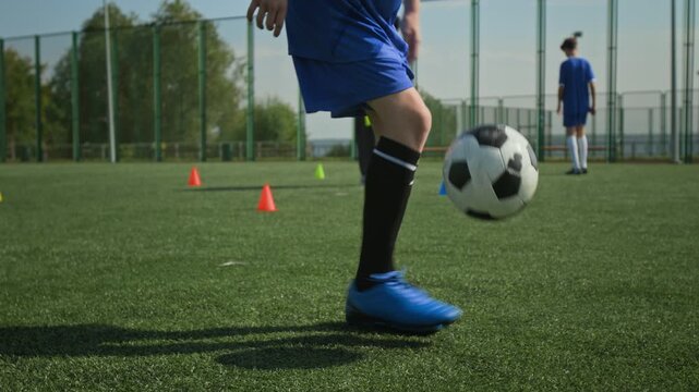 Close up of unrecognizable boy juggling football on pitch while his teammate and coach in background