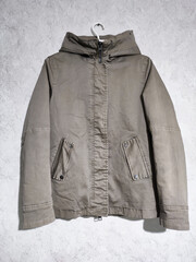 Fade olive green hooded parka jacket hangs on hanger isolated on gray wall background. Short winter khaki cotton parka with insulation. Military style casual women's coat. Army green outerwear  © Simona
