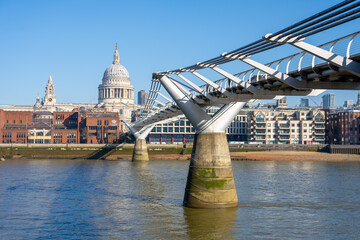 Millennium Bridge connects the north and south banks of the Thames. St. Paul's Cathedral rises majestically in the background on a clear day, showcasing London's skyline.
