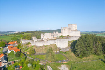 Drone captures an aerial view of the historic Rabi Castle ruins, showcasing its impressive stone structure amidst lush green fields and nearby residential areas in Czechia.