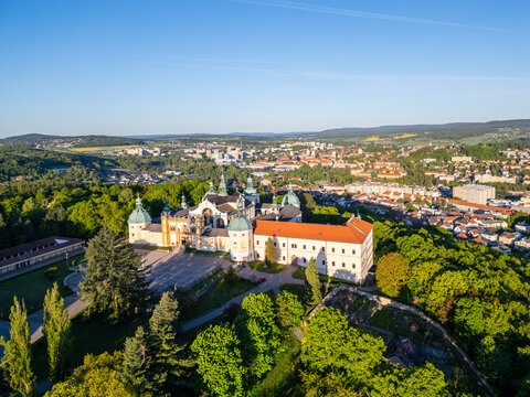 Holy Mountain in Pribram features a stunning Baroque complex surrounded by lush greenery, attracting many pilgrims. The sun illuminates the landscape, creating a serene atmosphere for visitors.