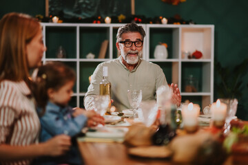 Grandfather holding wine bottle talking to family at thanksgiving dinner table