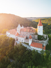 Obraz premium Krivoklat Castle stands majestically in Central Bohemia, showcasing its medieval architecture during a stunning sunset. The vibrant colors highlight its historic features against lush greenery.