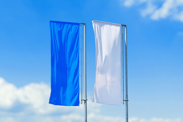 Pair of vertical flags in blue and white colors waving on poles against clear sky, outdoor advertising or event decoration.