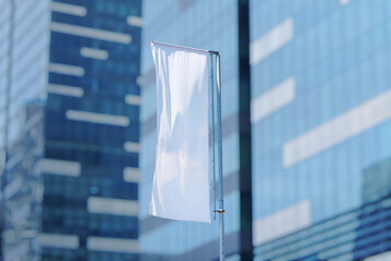 White vertical advertising flag waving on pole in front of modern glass building, outdoor corporate branding and business promotion concept.