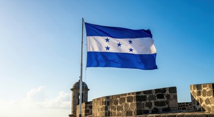 honduran flag waving against clear blue sky atop stone fortress of santa barbara wall. symbol of national pride and patriotism. travel, cultural heritage. honduras independence day