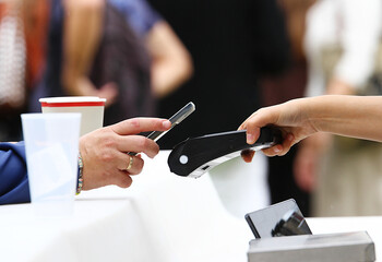 Datáfono tpv terminal punto de venta con lector pagando y cobrando virtual en comercio con teléfono móvil en la barra de un bar entre camarero y cliente comprador © Diego