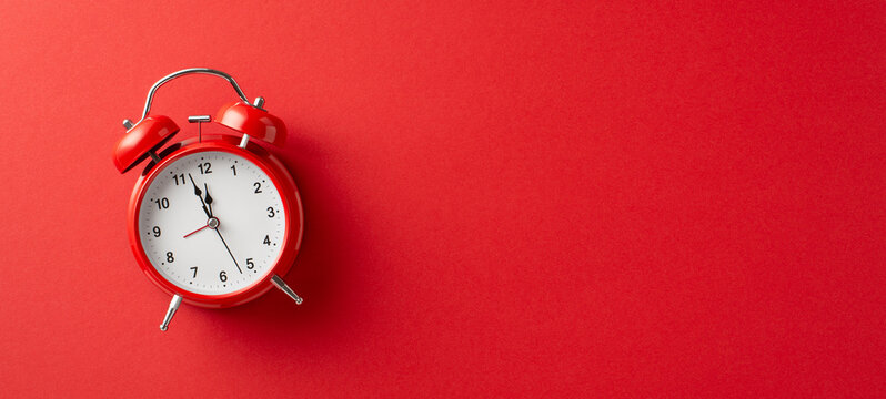 A bright red alarm clock sits on a rich red surface, conveying urgency and festive anticipation for Christmas and New Year celebrations; ideal for seasonal promotions and holiday mood imagery