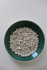 Uncooked dried white haricot beans in a bowl. Background pile of haricot beans (Phaseolus vulgaris).