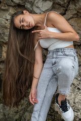 Beautiful woman in a white top and gray jeans poses on rocks in the mountains