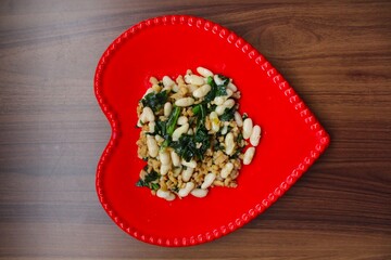 Vegetarian stew of white beans with spinach on wooden table. Close-up. Horizontal top view.