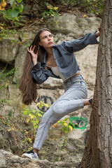 Beautiful woman in a white top and gray jeans poses on rocks in the mountains
