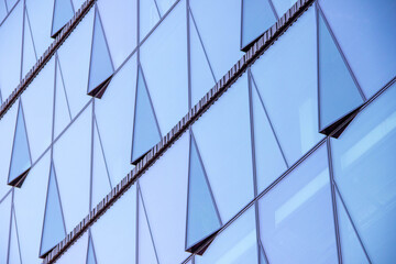 Obraz premium Modern architectural facade featuring geometric glass panels with angular shapes reflecting light, showcasing innovative design and contemporary aesthetics in urban environments