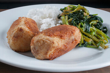 Potato and tuna croquettes filled with cheese, with steamed rice and spinach on the side, on a white plate, close-up or macro photography