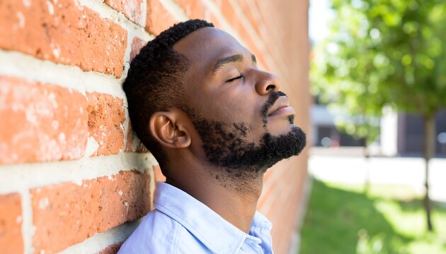 Man leaning against brick wall, thoughtful expression
