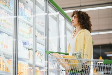 Customer choosing frozen food from refrigerated shelf in supermarket