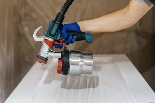 Skilled individual using a paint sprayer with a metallic container, applying paint to a smooth surface, showcasing the precision of the painting process in a workshop environment