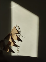 A close-up shot of a rustic, handmade brown paper bunting garland illuminated by a dramatic shaft of late afternoon sunlight against a textured, light-colored wall