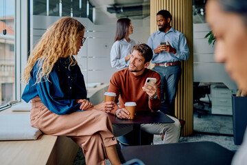Diverse business people gathering in a modern open-plan office during coffee break, talking and using smartphones