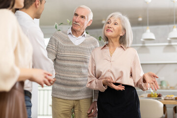 Fototapeta premium Elderly couple welcomes guests pair of son with girlfriend at home. After chatting and gatherings, men shake hands, say goodbye, thank you for pleasant evening.