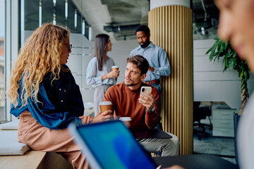 Young diverse business team members communicating during a coffee break, holding takeaway cups and smartphones in a contemporary office setting