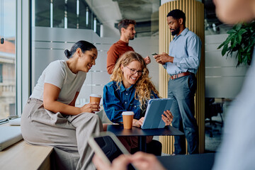 Business people enjoying coffee, smiling, and using digital tablet during work break in a modern office